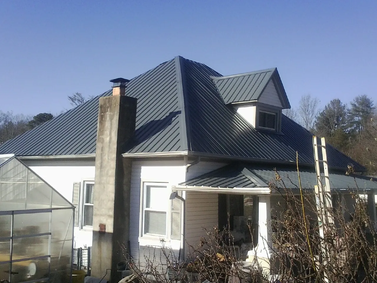 Dark blue standing seam metal roof on a white farmhouse with dormer — Slate & Tile Roof Repair by Roofing Brothers in Eighty Eight