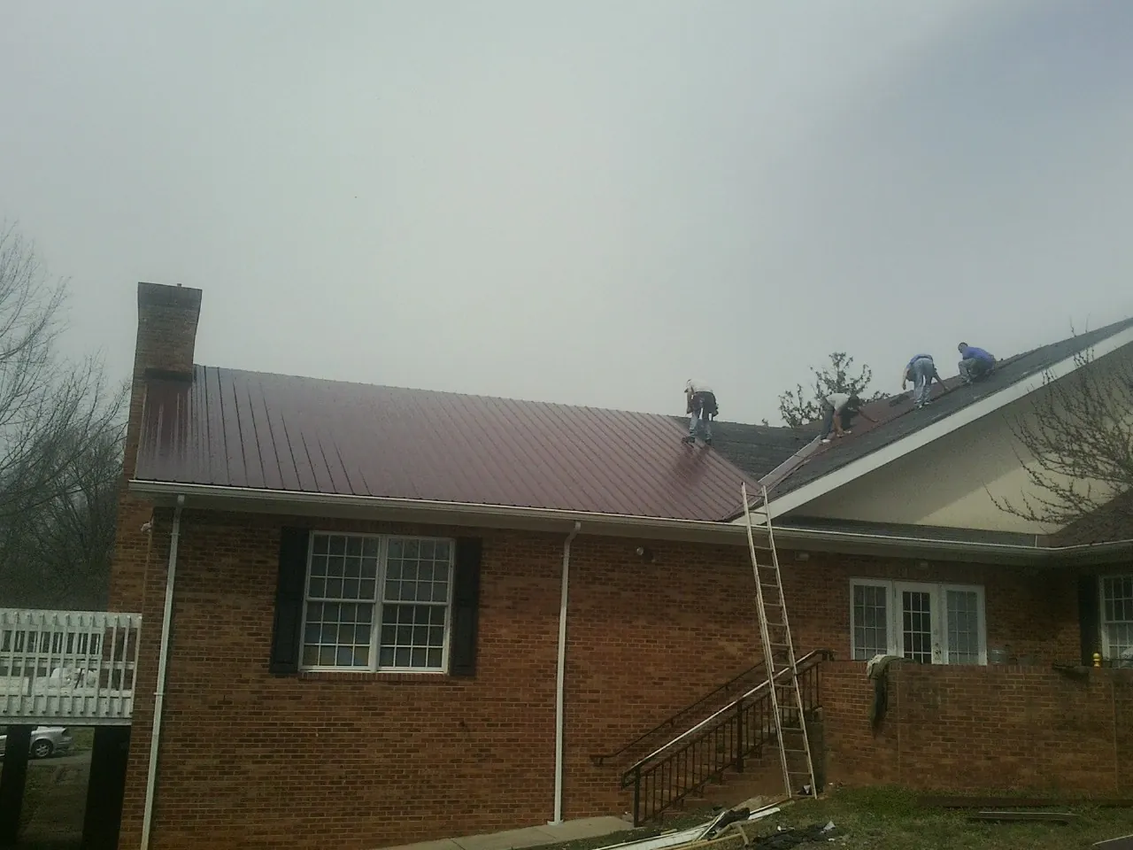 Crew setting red metal roofing panels on a brick home in Eighty Eight
