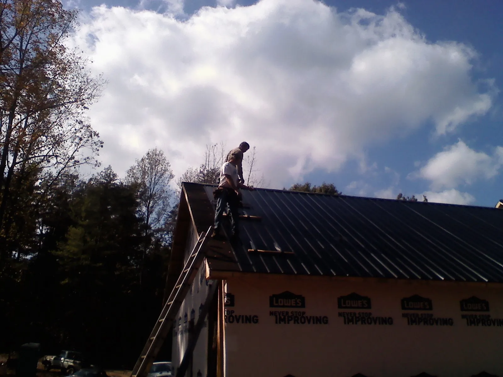 Roofer fastening dark metal panels high against a cloudy sky, from a Roof Inspection job in Eighty Eight