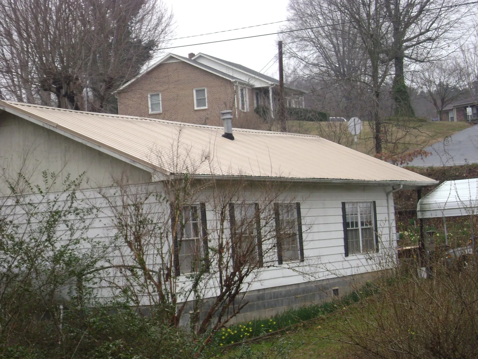 Tan metal roof on a white sided house set into a hillside — Commercial Roofing by Roofing Brothers in Eighty Eight
